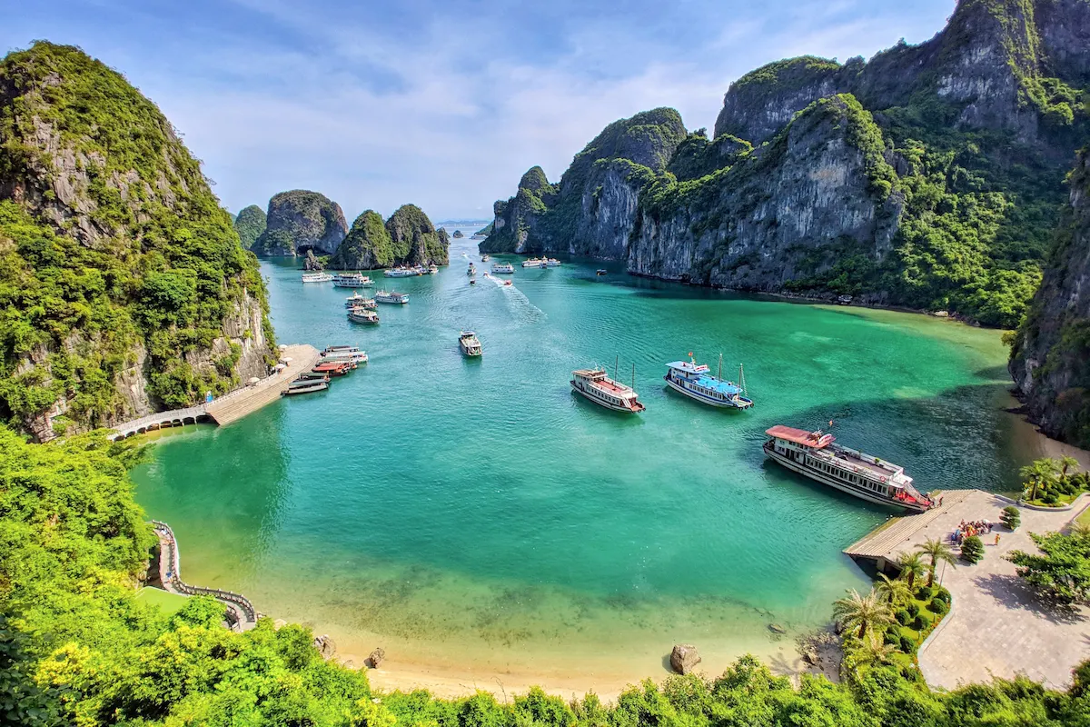 Halong Bay cruise boats anchored by limestone karsts and sandy beach