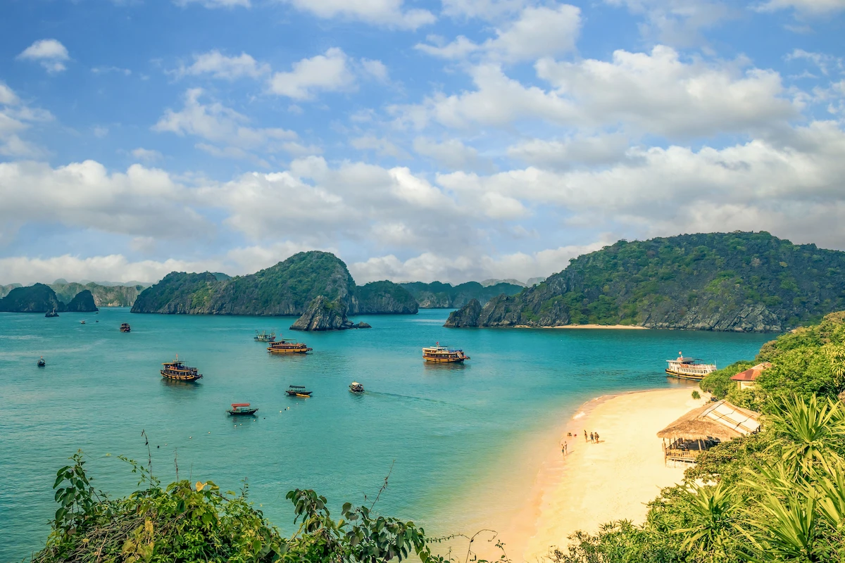 Turquoise Lan Ha Bay with cruise boats, limestone islands, and sandy beach