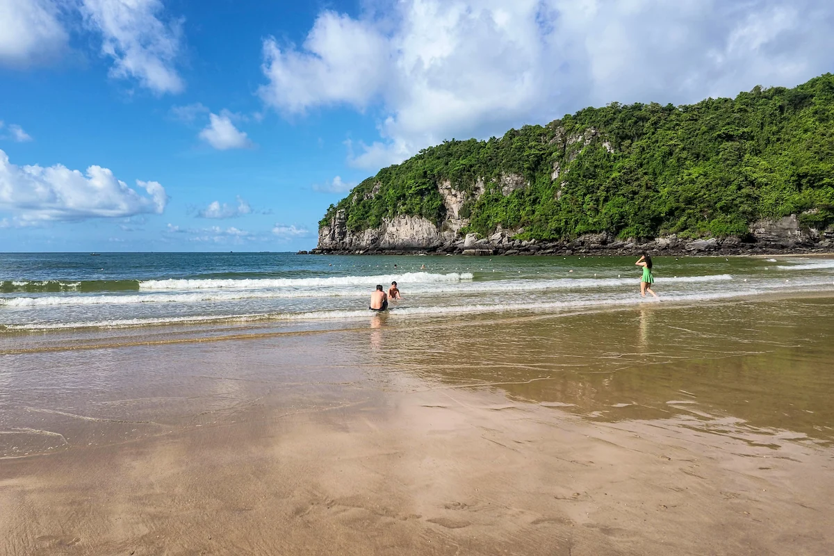 Tourists enjoying shallow waves on a sandy Cat Ba Island beach
