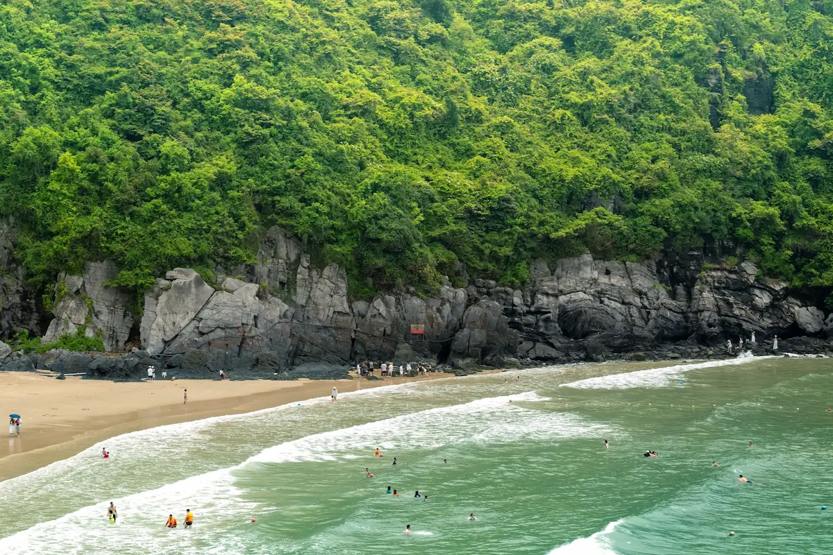 Swimmers at a sandy Cat Ba Island beach backed by green cliffs