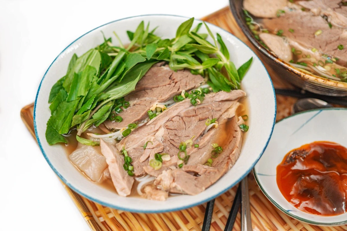 A bowl of Hanoi beef pho topped with fresh herbs and sliced beef