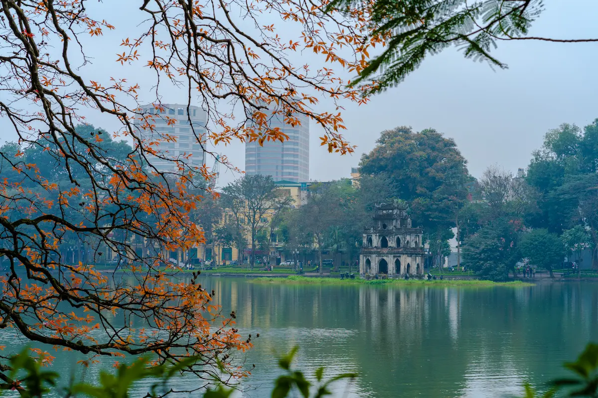 Turtle Tower stands beside Hoan Kiem Lake, framed by autumn foliage in Hanoi