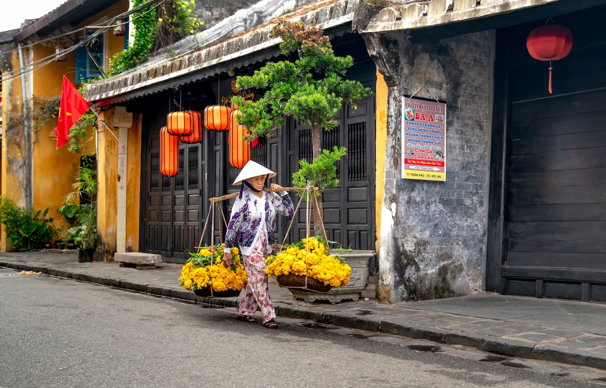 Woman carrying yellow flowers along a historic Hoi An street