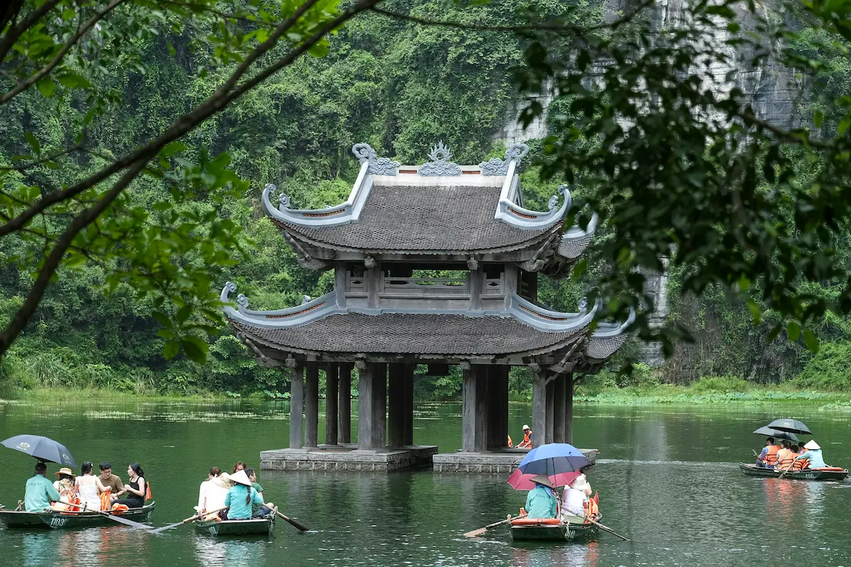 Visitors take a scenic Trang An boat tour past a traditional pavilion and limestone scenery