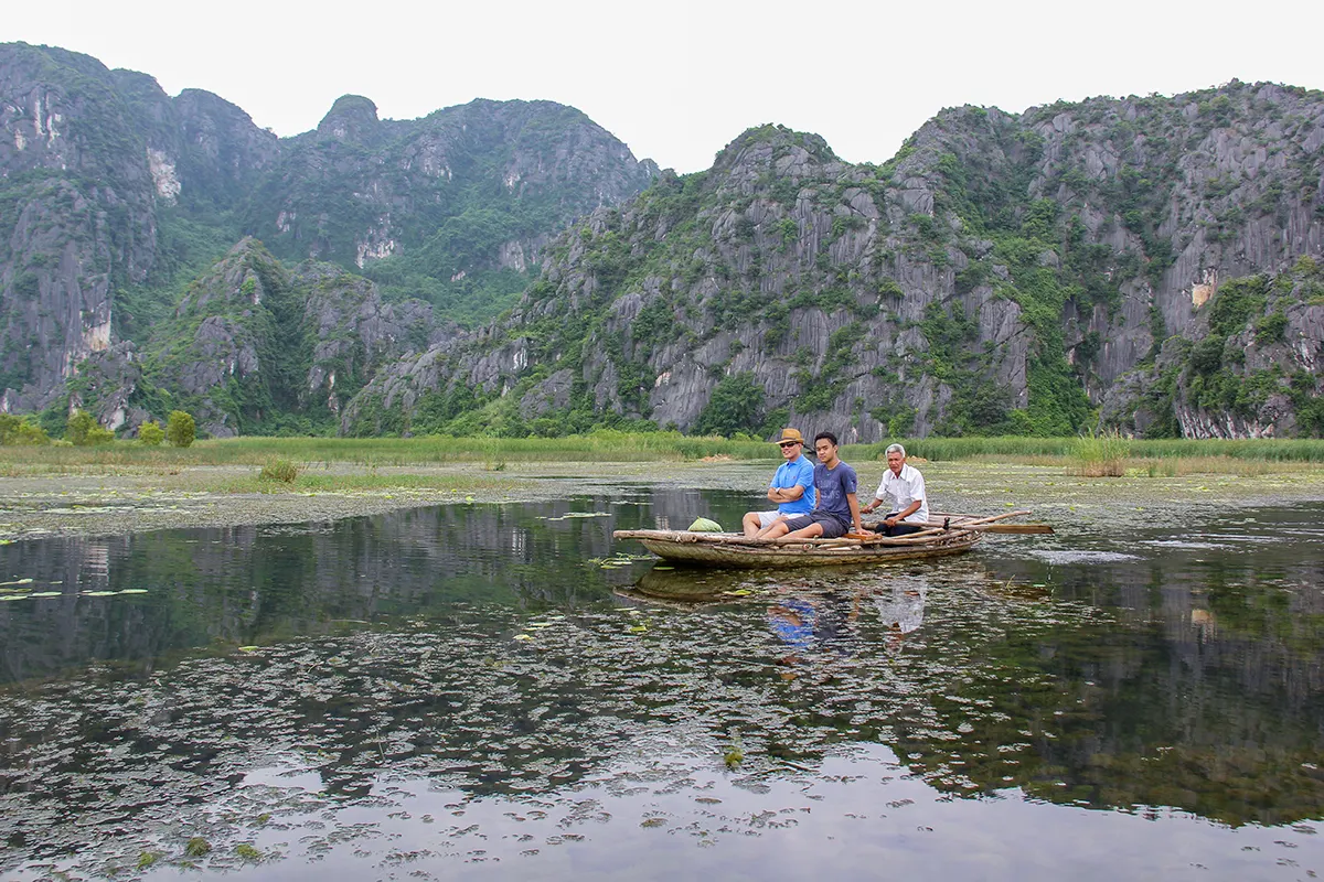 Visitors travel by traditional boat beneath the limestone cliffs of Van Long Nature Reserve